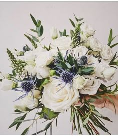 a bouquet of white flowers and greenery is held by someone's hand in front of a wall