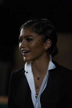 a woman wearing a black suit and white shirt with a birdcage veil on her head