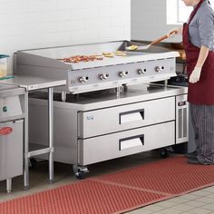 a woman in an industrial kitchen preparing food on the stove top and grills behind her