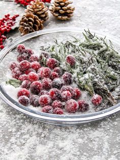 berries and pine cones covered in snow on a glass platter next to evergreen cones