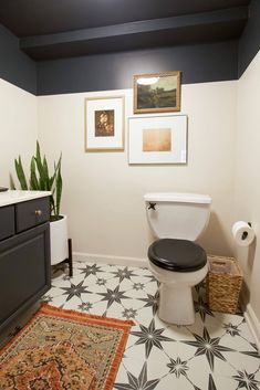 a white toilet sitting next to a black and white sink in a room with pictures on the wall