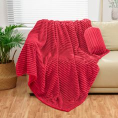 a red blanket sitting on top of a couch next to a potted plant