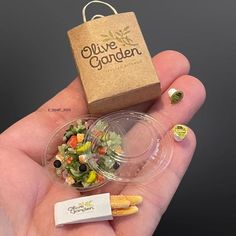 a hand holding a small plastic container filled with salad and chips next to a cardboard box