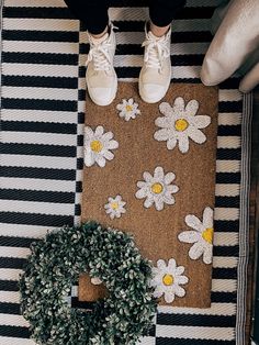 a person standing on top of a rug next to a wreath and door mat with daisies