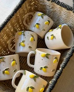 four white mugs with yellow lemons on them sitting in a wicker basket