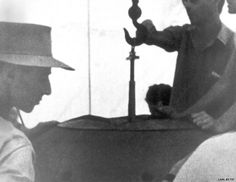 black and white photograph of two men in hats looking at an object on a table