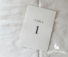 a table number is placed on top of a white linen covered bed sheet with the word table 1 printed on it