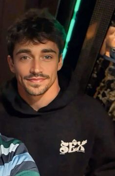 a man in a black hoodie is smiling at the camera