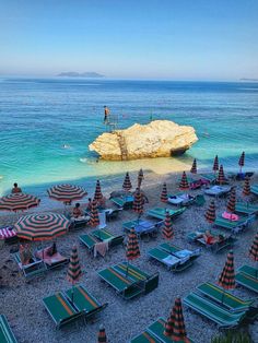 there are many beach chairs and umbrellas on the sand near the water's edge