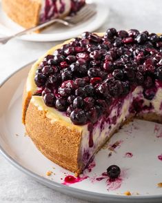 a blueberry cheesecake on a white plate with a slice cut out and ready to be eaten