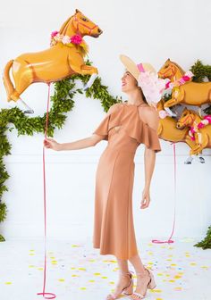 a woman in a dress and hat holding two horse balloons