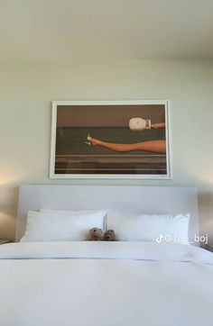 a bed with white sheets and pillows in front of a painting on the wall above it