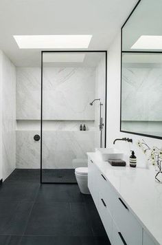 a white bathroom with black tile flooring and skylights above the shower area is shown