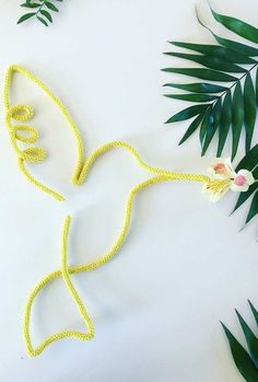 a yellow string necklace with white flowers and green leaves on the table next to it