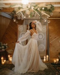 a woman in a white dress standing under a chandelier with candles and flowers