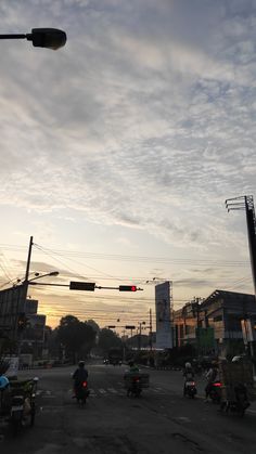 people riding motorcycles down the street at dusk with traffic lights and buildings in the background