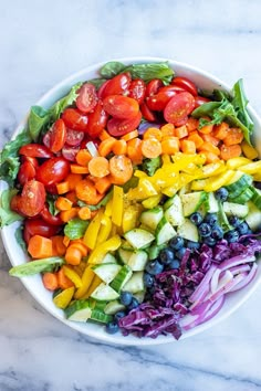 a bowl filled with lots of different types of vegetables on top of a marble table