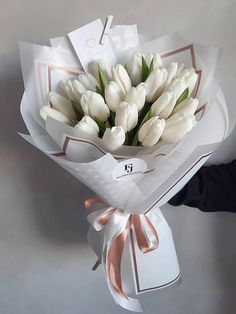 a bouquet of white tulips wrapped in paper and tied with a ribbon, held by someone's hand