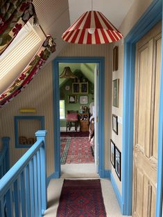 the hallway is decorated in blue and red with pictures on the wall, rugs hanging from the ceiling