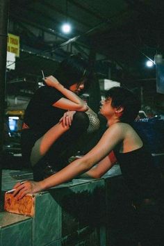 two people sitting on top of a wooden box in a warehouse area, one holding the other's leg