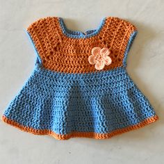 a crocheted blue and orange dress with a flower on the front, sitting on a white surface