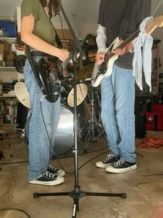 two people standing in front of a microphone with guitars on the floor and one person holding an electric guitar