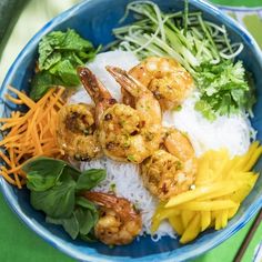 a blue bowl filled with rice and shrimp on top of a green table next to vegetables