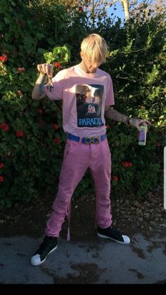 a man in pink pants and a t - shirt holding a skateboard with his right hand