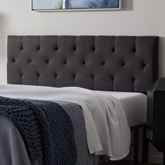 a bed with a gray headboard and white sheets in a bedroom next to a painting on the wall