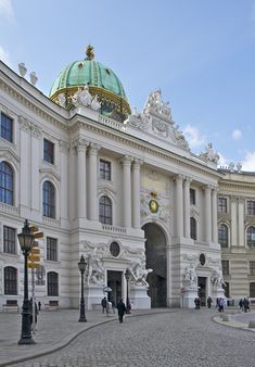 a large white building with a green dome on top and people walking in front of it