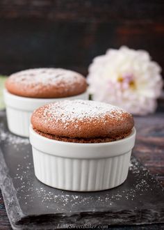 two chocolate cookies sitting on top of a black slate tray next to a white flower