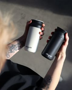 a person holding two coffee mugs in one hand and another with tattoos on their arm