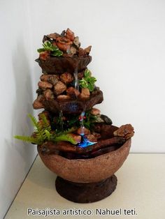 a water fountain with rocks and plants on it's sides, in a bowl