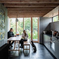 two people sitting at a table with a dog in front of them and a cat on the floor