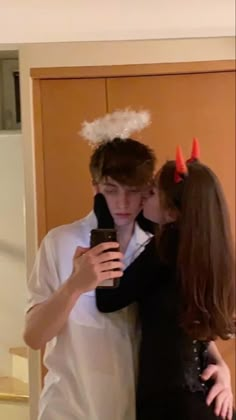 two people dressed up as devil and demon kiss each other's forehead while standing in front of a door