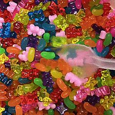 a bowl filled with lots of colorful gummy bear candies next to a plastic spoon