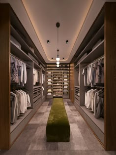 a walk - in closet filled with lots of clothes on shelves next to a green bench