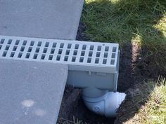 a drain in the ground next to a sidewalk with a white pipe sticking out of it