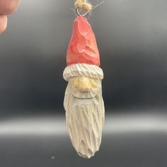 a ceramic santa clause ornament being held by a person's hand and wearing a red hat