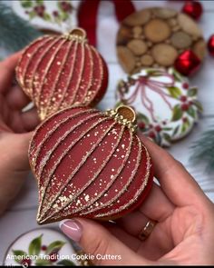 two red ornaments are being held by someone