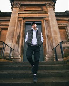 a man standing in front of a doorway with his hands in his pockets and wearing a vest