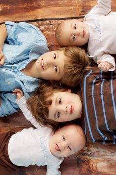 three young boys laying on top of each other in front of a wooden bench with their arms around one another