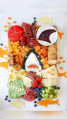 an assortment of cheeses, crackers, fruit and other items are arranged on a white surface