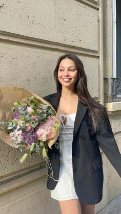 a woman holding a bouquet of flowers in front of a building