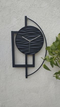 a clock that is on the side of a white wall next to a potted plant