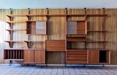 an empty room with wooden shelves and drawers on the wall next to a tiled floor