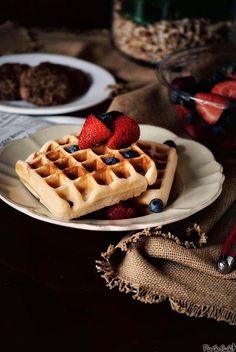 waffles with strawberries and blueberries are on a plate next to other breakfast foods