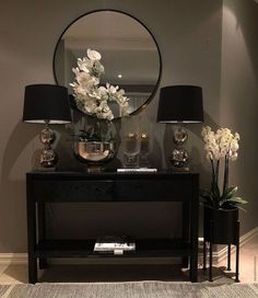 a black table topped with two lamps next to a mirror and vase filled with flowers