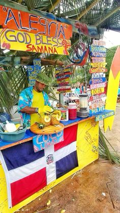 a man cooking food on top of a flag covered stand in front of palm trees