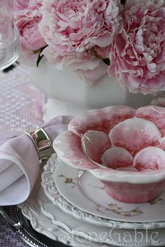 pink peonies are in a white bowl on a table with plates and napkins